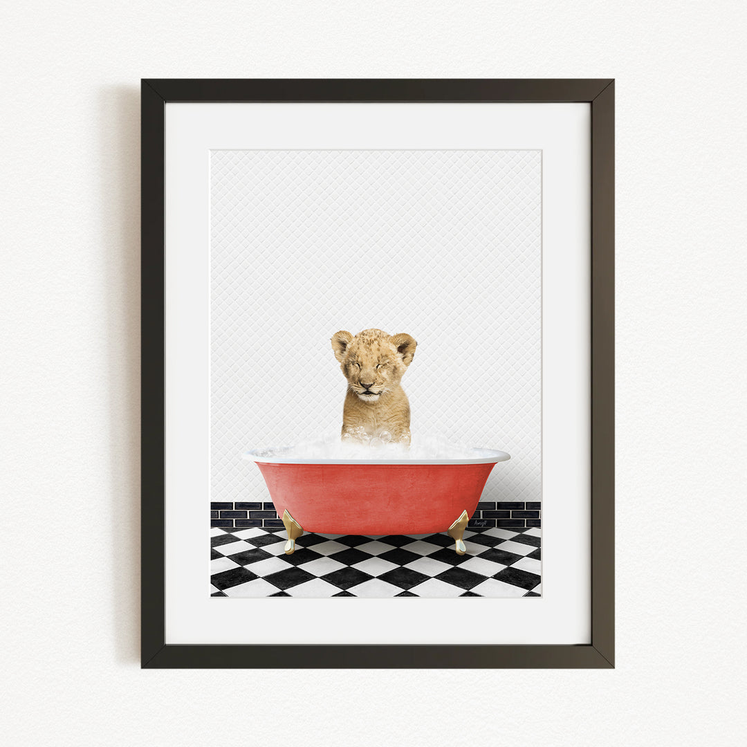 A young lion cub sitting in a red bathtub filled with water, surrounded by a black and white checkered floor.