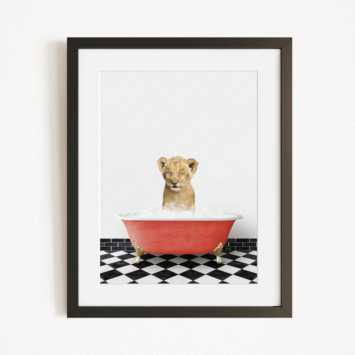 A young lion cub sitting in a red bathtub filled with water, surrounded by a black and white checkered floor.