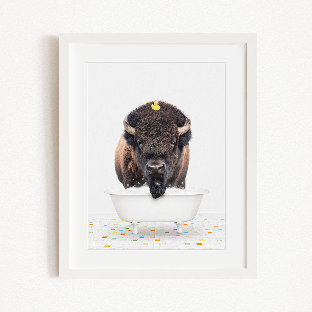 A buffalo with a yellow rubber duck perched on its head is standing in a white bathtub, surrounded by colorful tiles on the floor.