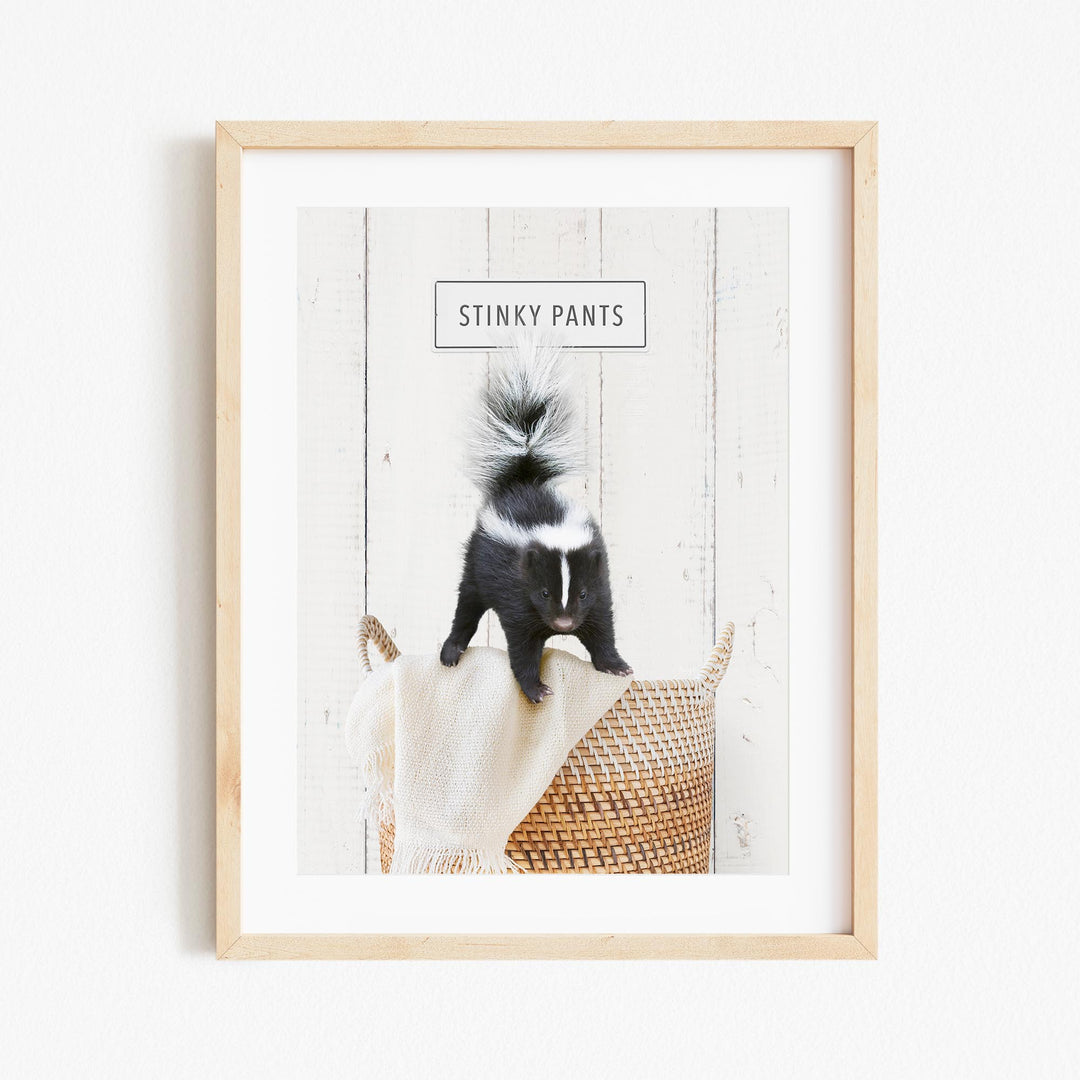 A black and white skunk sitting on a woven basket, with the text "STINKY PANTS" displayed above it.