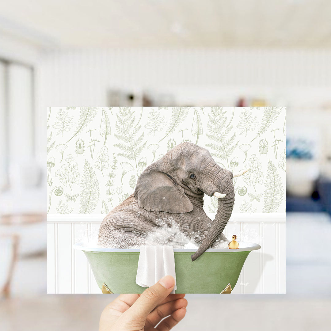 A hand holds up a framed image depicting an elephant sitting in a green bathtub, surrounded by a fern-patterned wall.