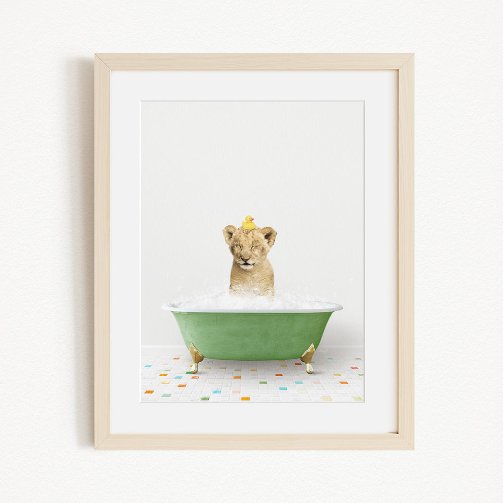 A young lion cub is sitting in a green bathtub filled with water, with a yellow rubber duck floating on the water.