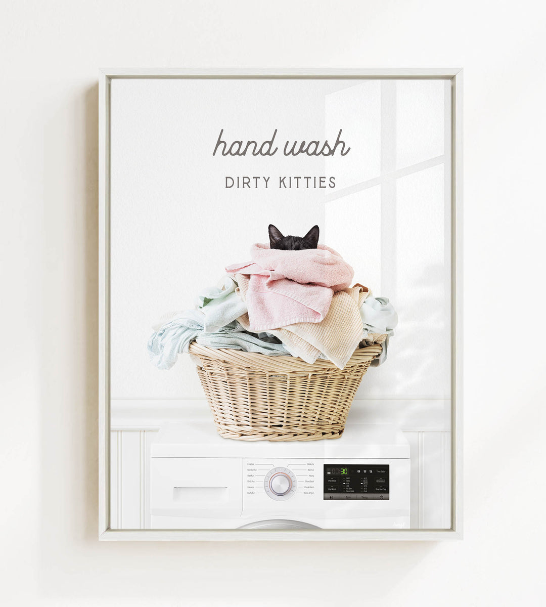 A framed image depicting a cat sitting in a basket filled with laundry, with the text "hand wash dirty kitties" above the basket.