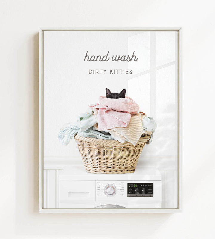 A framed image depicting a cat sitting in a basket filled with laundry, with the text "hand wash dirty kitties" above the basket.