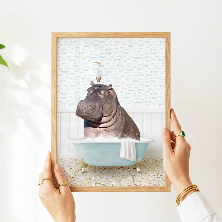 A person's hands are holding a framed image of a hippopotamus sitting in a bathtub filled with water and bubbles.
