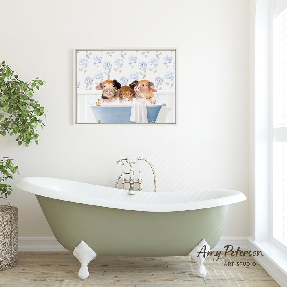 A framed image of three adorable hamsters sitting in a bathtub is displayed on the wall above a green clawfoot bathtub in a bright, white-walled bathroom.
