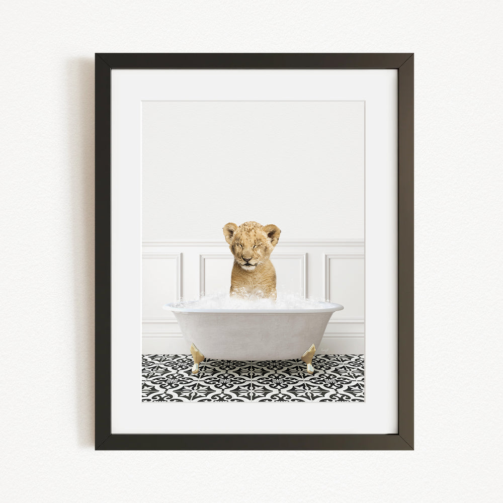 A young lion cub sitting in a white bathtub filled with water, surrounded by a black and white patterned rug.