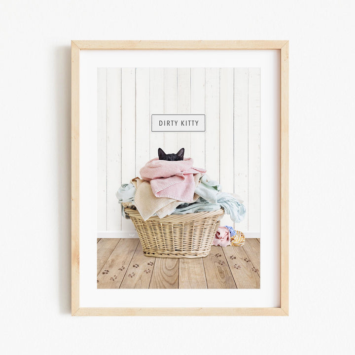 A framed image of a cat sitting in a basket filled with clothes, with the text "Dirty Kitty" displayed above the basket.
