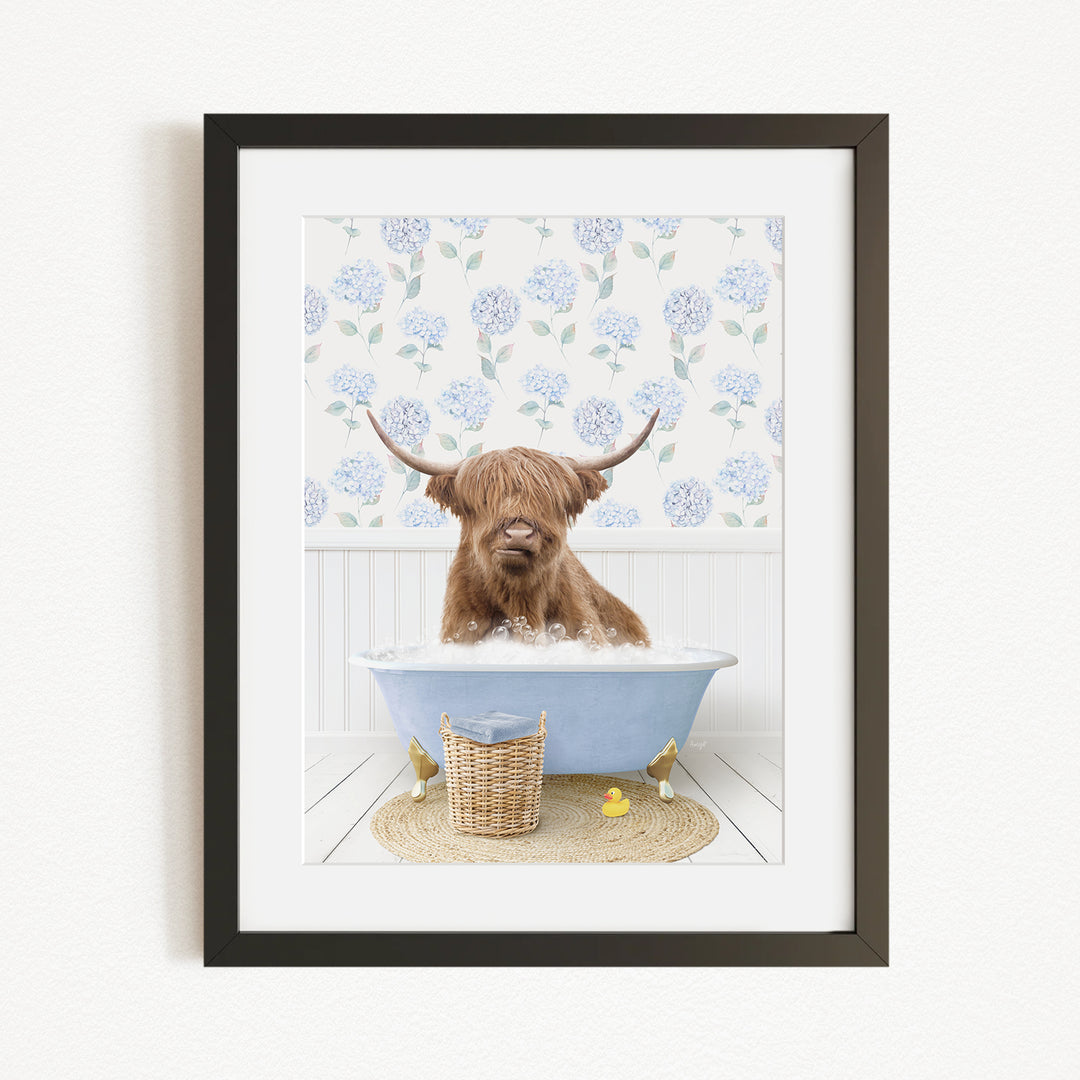 A brown cow with long horns is sitting in a blue bathtub filled with bubbles, surrounded by a floral patterned wall and a basket of rubber ducks.