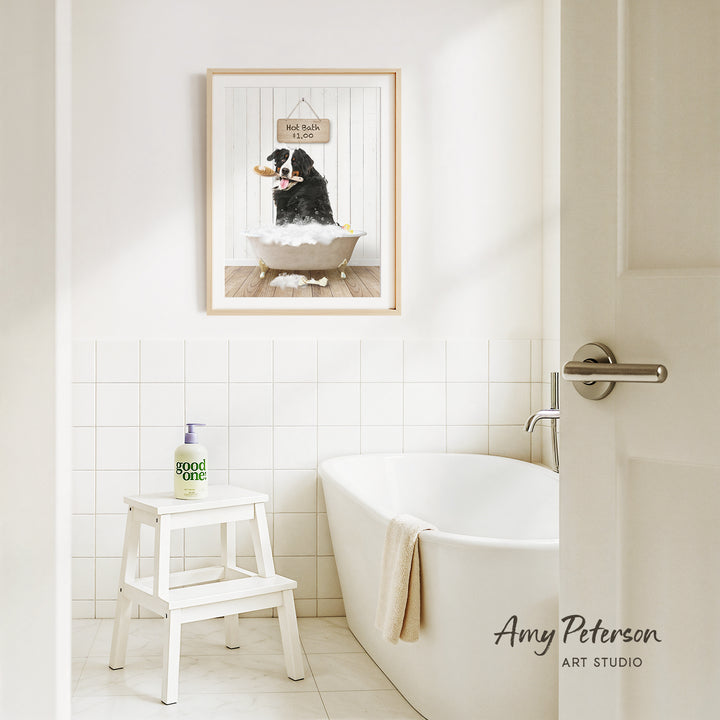 A framed picture of a dog sitting in a bathtub, with a sign above it that says "Hot Bath $1.00", is hanging on the wall above a white bathtub in a bathroom.