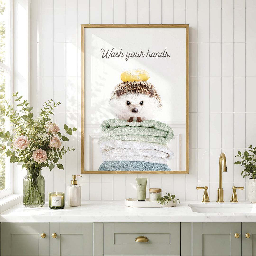 a bathroom with a framed poster of a hedgehog sitting on a stack of towels, accompanied by a vase of flowers and a candle on the counter.