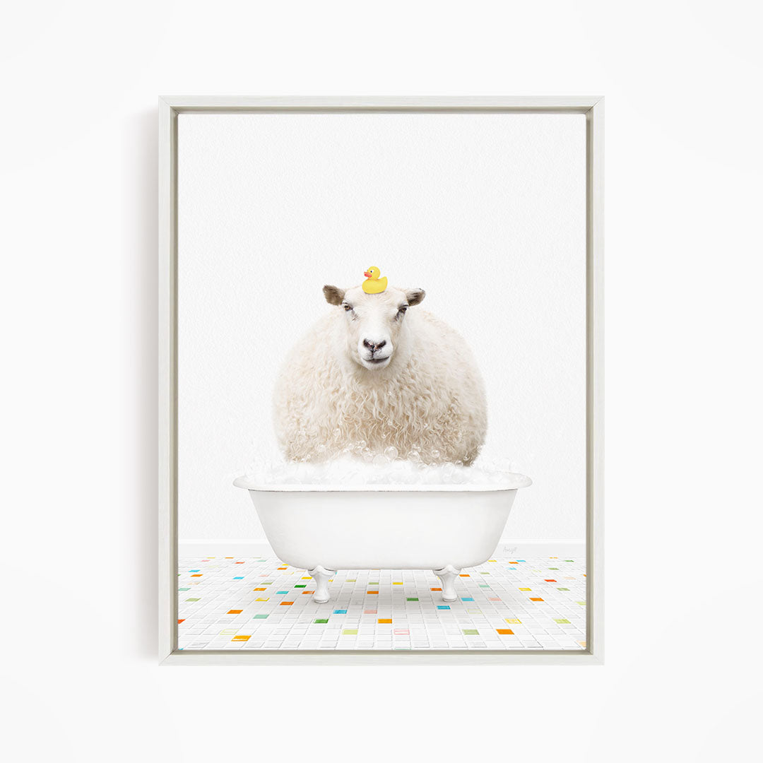 A fluffy white sheep sits in a white bathtub filled with bubbles, with a yellow rubber duck perched on its head.