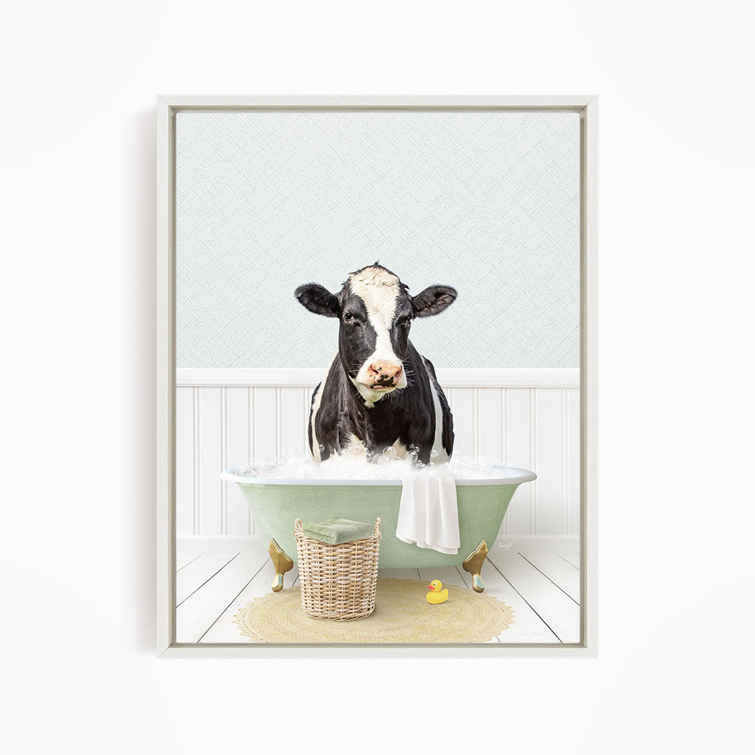 A black and white cow is sitting in a green bathtub filled with water, surrounded by a yellow rubber duck and a basket.