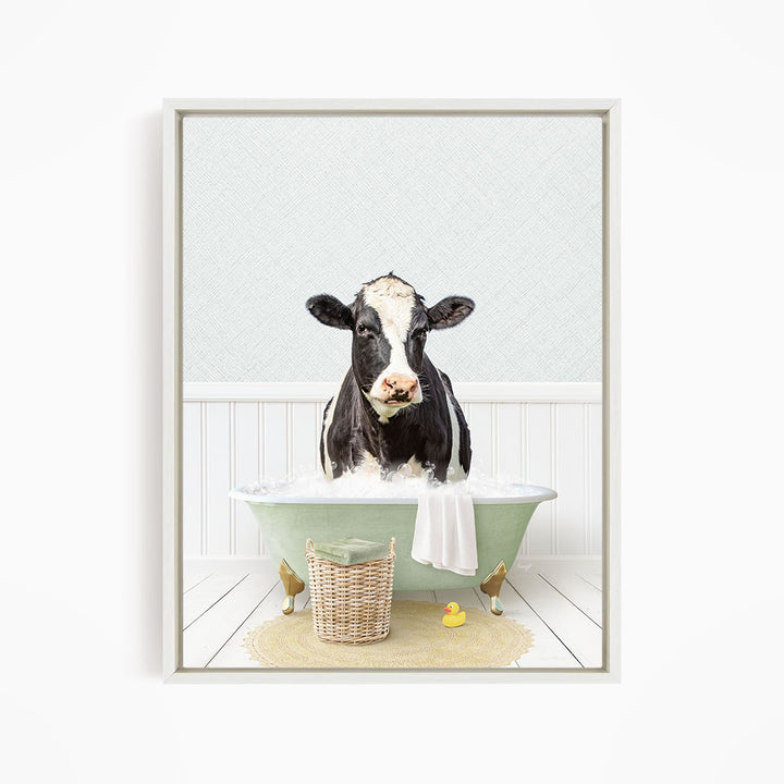 A black and white cow is sitting in a green bathtub filled with water, surrounded by a yellow rubber duck and a basket.