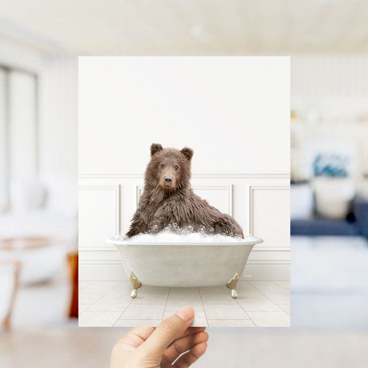 A brown bear sitting in a white bathtub filled with bubbles, with a blurred background suggesting a bathroom setting.