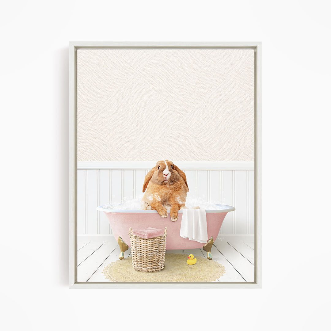 A brown rabbit sitting in a pink bathtub filled with bubbles, surrounded by a yellow rubber duck and a wicker basket.