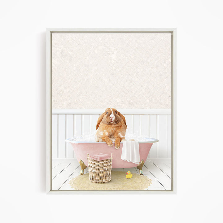 A brown rabbit sitting in a pink bathtub filled with bubbles, surrounded by a yellow rubber duck and a wicker basket.