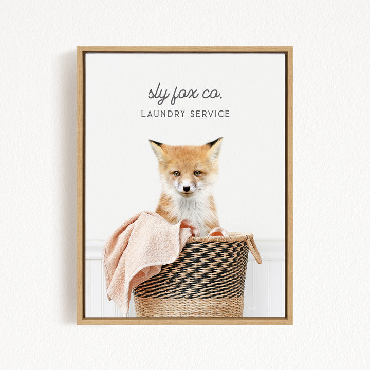 A framed image of a young fox sitting in a woven laundry basket, with the text "sky fox co. Laundry service" displayed above the fox.
