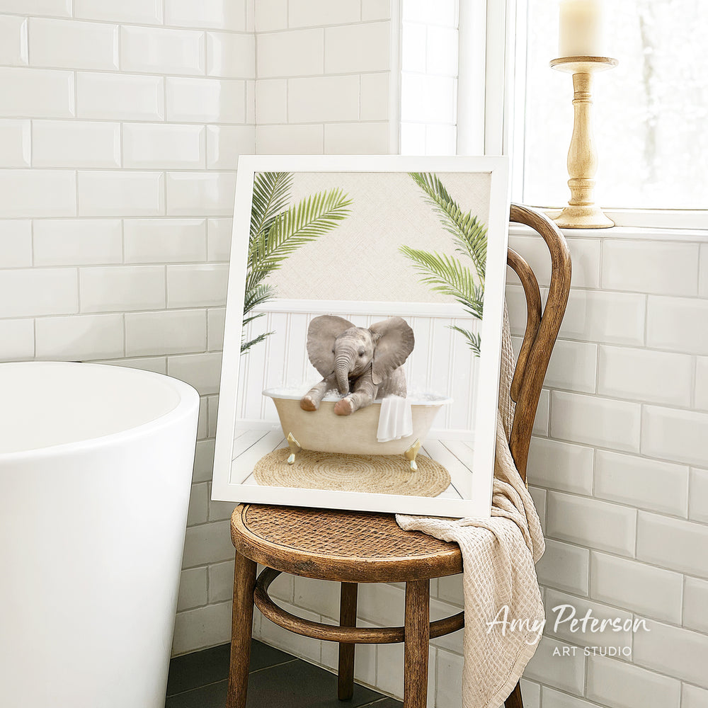 A framed image of two elephants sitting in a bathtub, surrounded by green leaves, is displayed on a wooden chair in a bathroom setting.