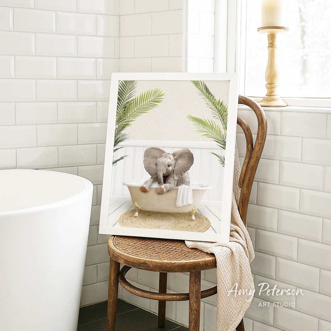 A framed image of two elephants sitting in a bathtub, surrounded by green leaves, is displayed on a wooden chair in a bathroom setting.