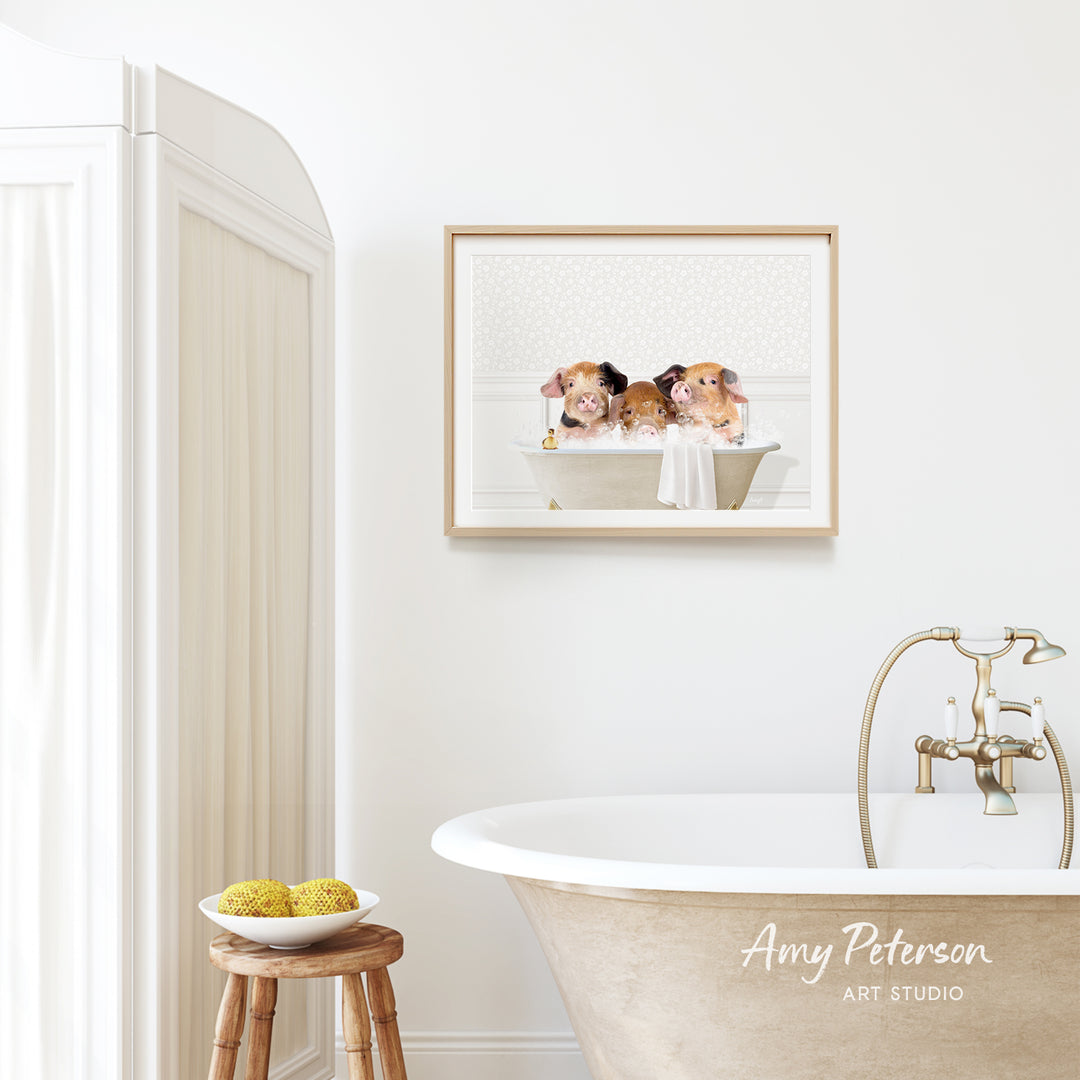 A framed image of three pigs sitting in a bathtub is hanging on a white wall above a freestanding bathtub in a bathroom.