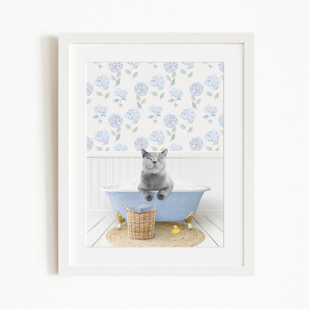 A gray cat sitting in a blue bathtub, surrounded by a floral patterned wall, a basket, and a yellow rubber duck.