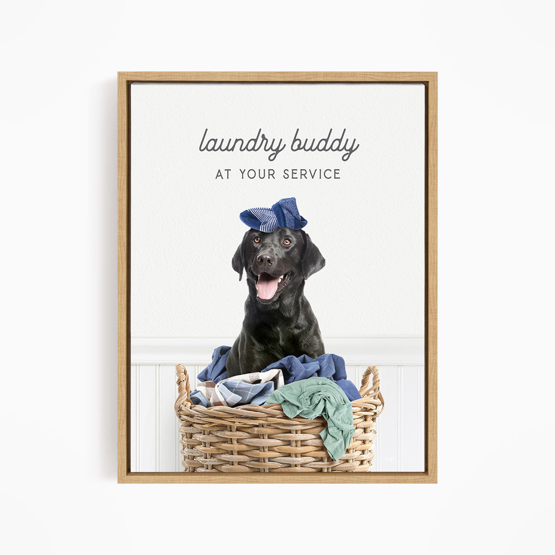 A black dog wearing a blue hat sits in a wicker laundry basket filled with clothes.