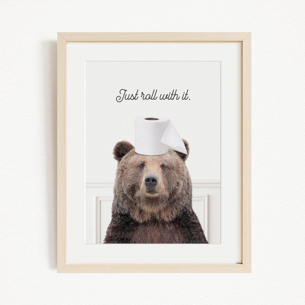 A framed image of a brown bear wearing a roll of toilet paper on its head, with the text "Just roll with it" above the bear.