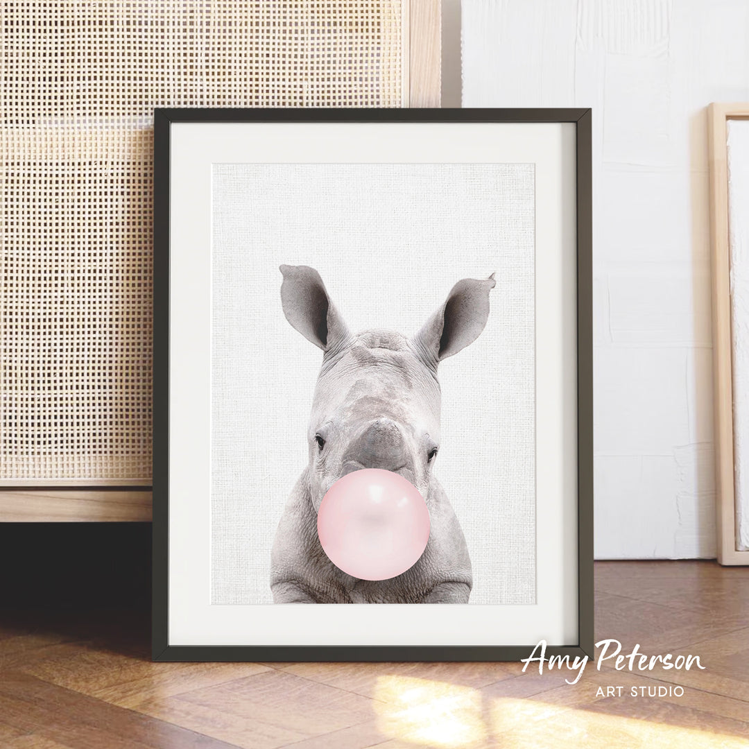 A framed image of a rhinoceros blowing a bubble with a pink bubble gum bubble.