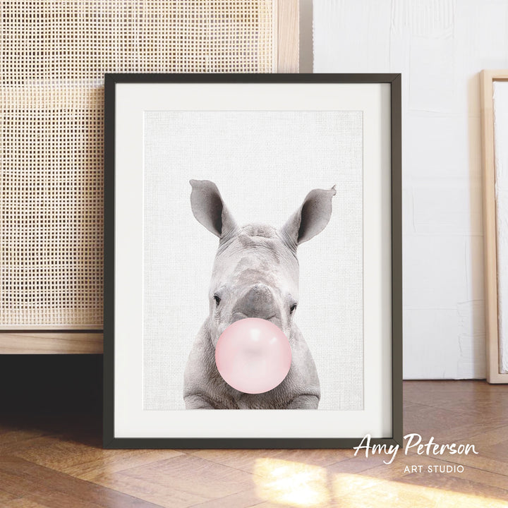 A framed image of a rhinoceros blowing a bubble with a pink bubble gum bubble.