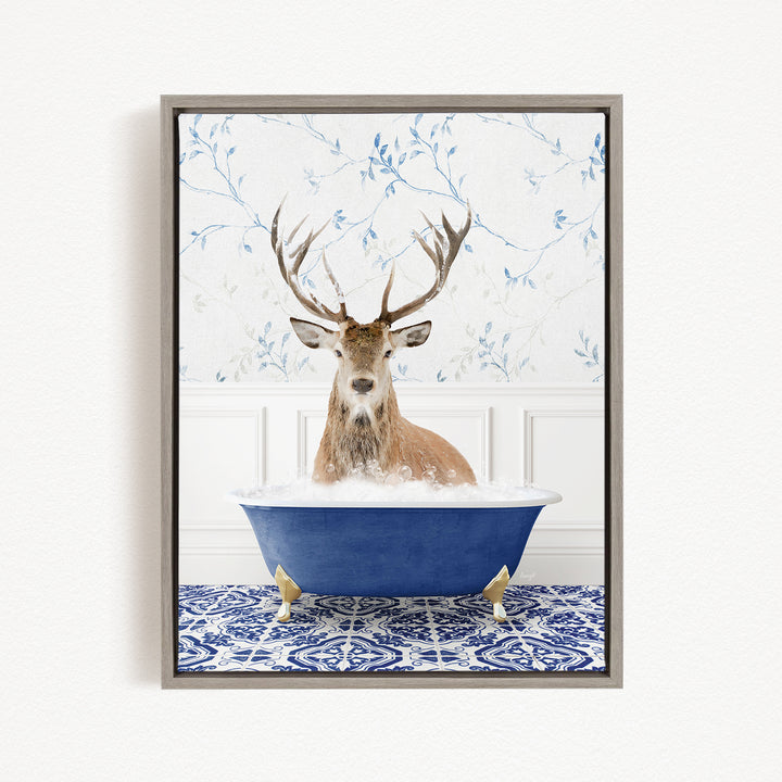 A deer with large antlers is sitting in a blue bathtub, surrounded by a patterned tile floor and a floral wallpaper background.