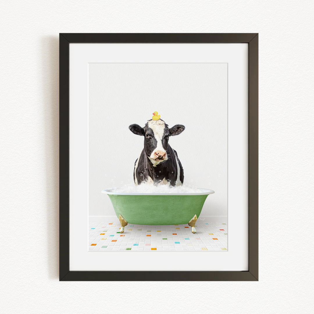 A black and white cow is sitting in a green bathtub filled with bubbles, with a yellow duck perched on its head.