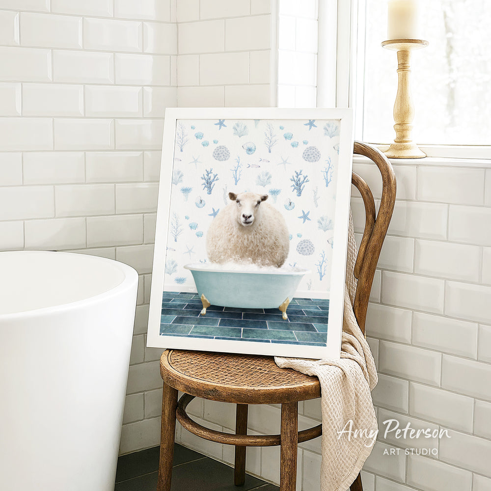 A framed image of a sheep sitting in a bathtub, surrounded by blue and white floral patterns, is displayed on a wooden chair in a bathroom setting.