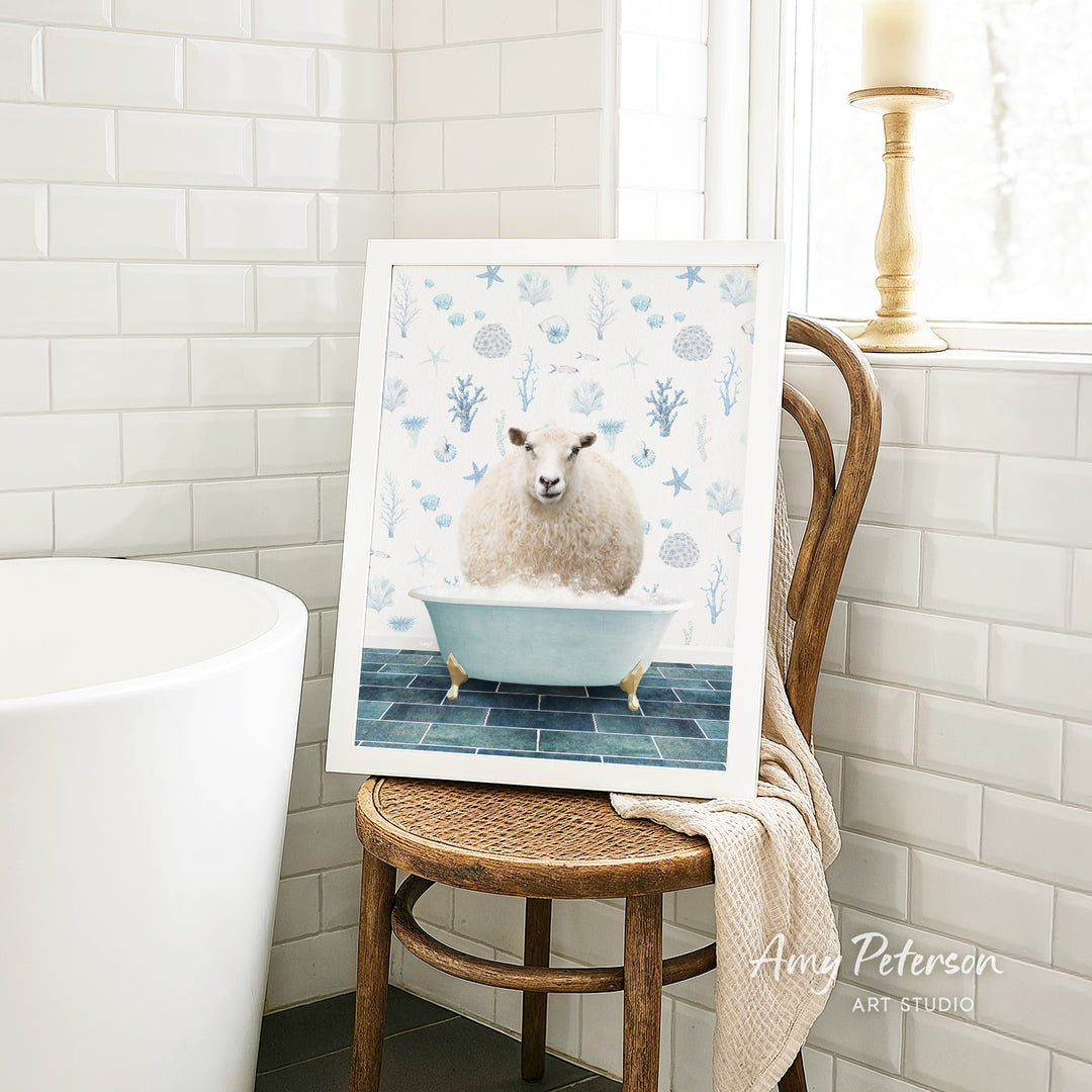 A framed image of a sheep sitting in a bathtub, surrounded by blue and white floral patterns, is displayed on a wooden chair in a bathroom setting.