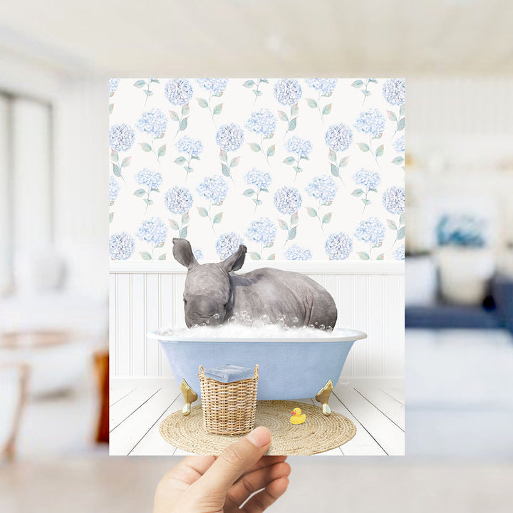 A rhinoceros is sitting in a blue bathtub filled with bubbles, surrounded by a floral patterned wall and a yellow rubber duck.