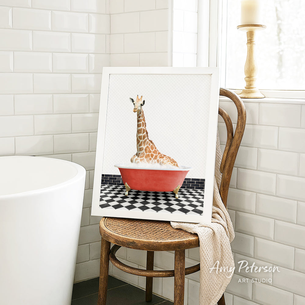A framed image of a giraffe sitting in a red bathtub, placed on a wooden chair in a bathroom setting.
