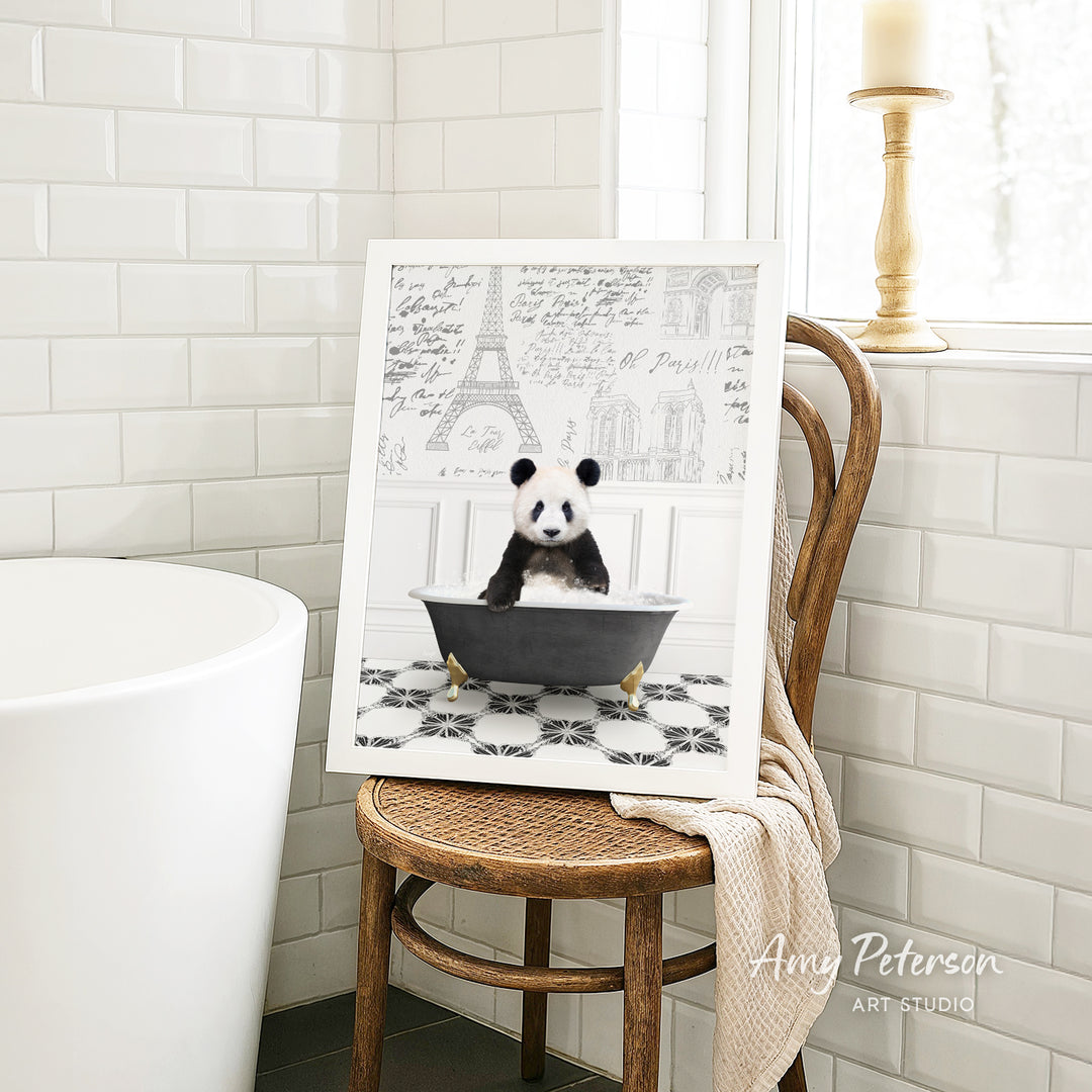 A framed image of a panda sitting in a bathtub is displayed on a wooden chair in a bathroom setting.