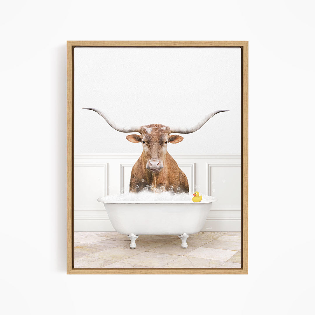 A brown steer with long horns is sitting in a white bathtub, with a yellow rubber duck floating in the water.
