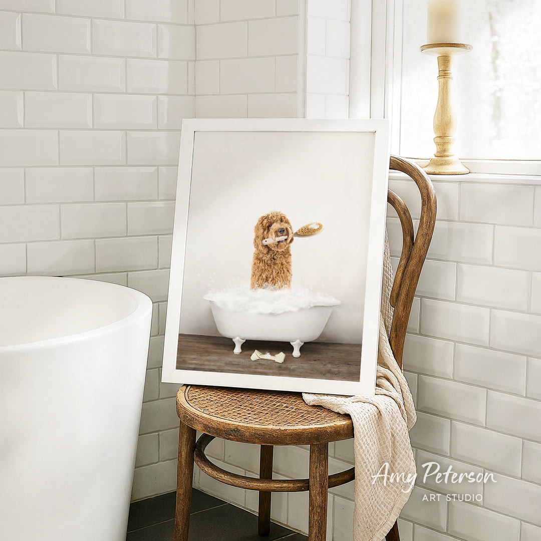 A framed photograph of a dog sitting in a bathtub, with a towel draped over the back of a wooden chair in a bathroom setting.