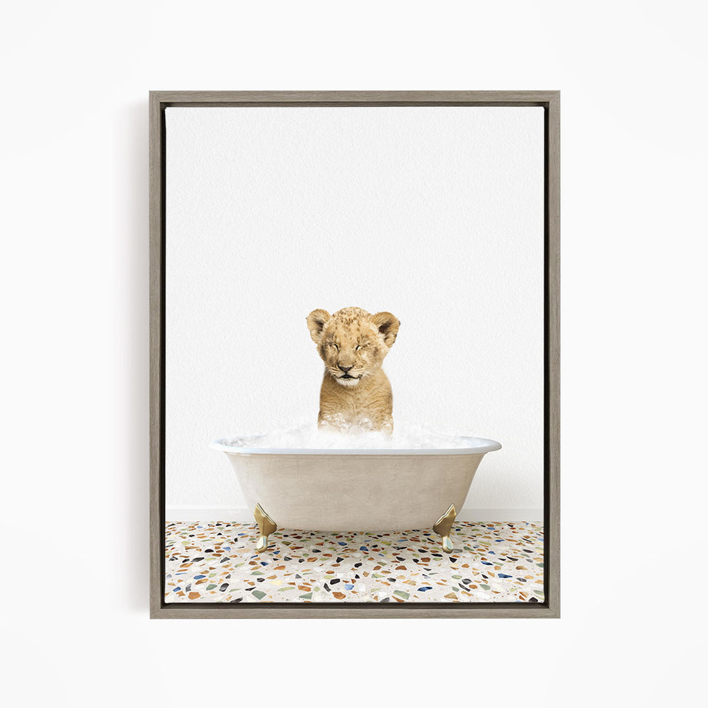 A young lion cub sitting in a white bathtub filled with water, looking up at the camera.