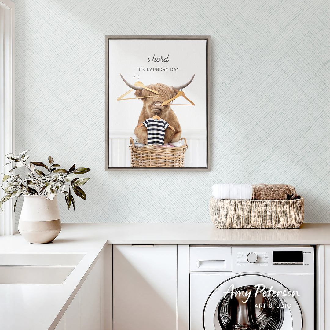 a framed poster of a cow sitting in a basket, with a humorous caption that reads "It's laundry day". The poster is displayed above a white sink and a white washing machine, creating a playful and lighthearted atmosphere in the room.