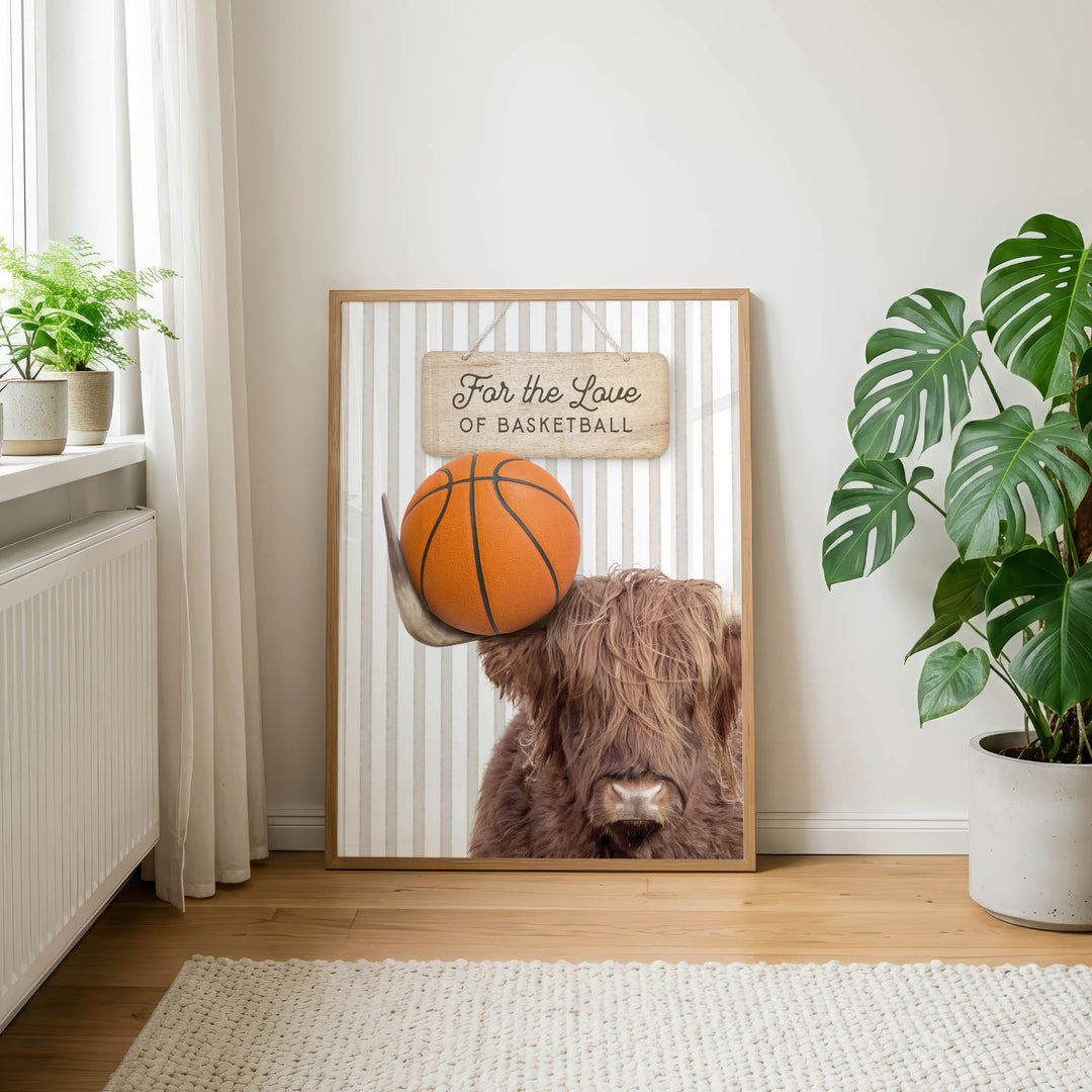 a framed poster with a close-up of a brown cow's head holding a basketball, accompanied by a wooden sign that reads "For the Love of Basketball".