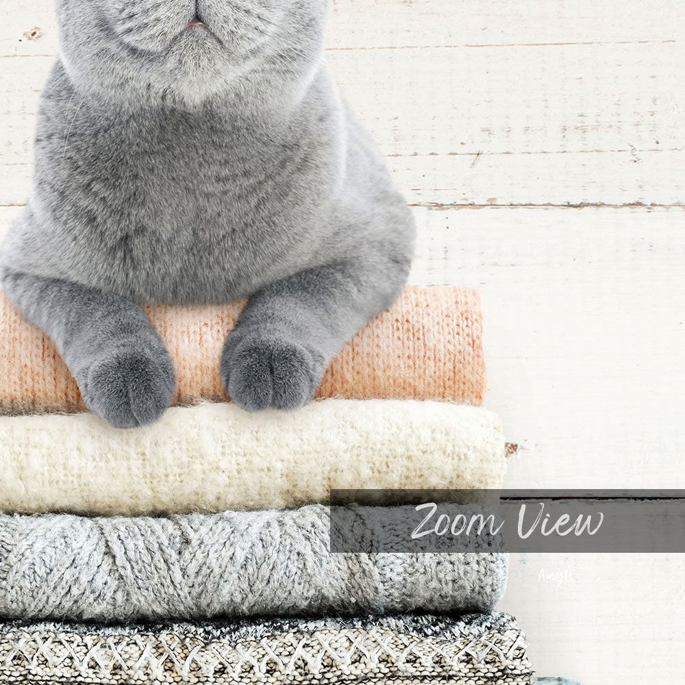 A gray cat sitting on top of a stack of variously colored and patterned blankets.