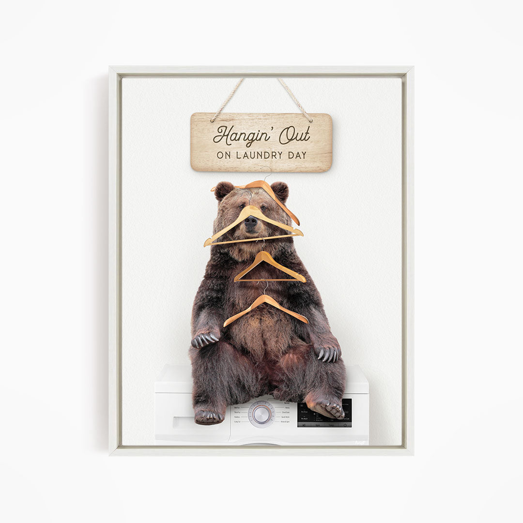 A framed image of a bear sitting on a washing machine, with a wooden sign above it that says "Hangin' Out on laundry day".