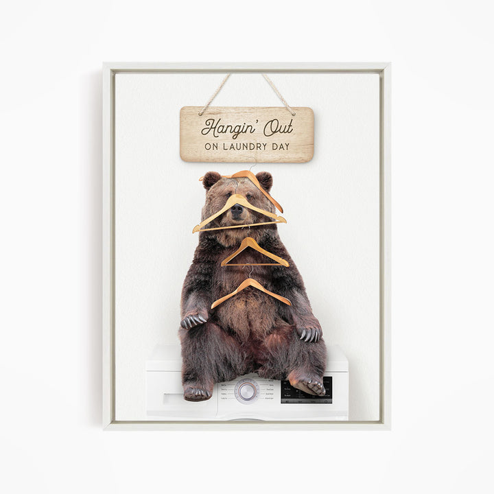 A framed image of a bear sitting on a washing machine, with a wooden sign above it that says "Hangin' Out on laundry day".
