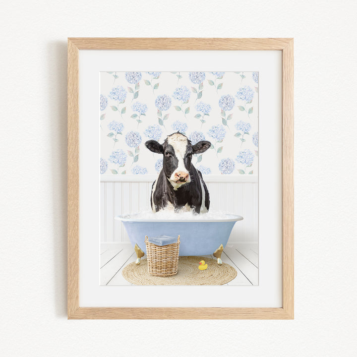 A black and white cow is sitting in a blue bathtub filled with water, surrounded by a floral pattern on the wall behind it.