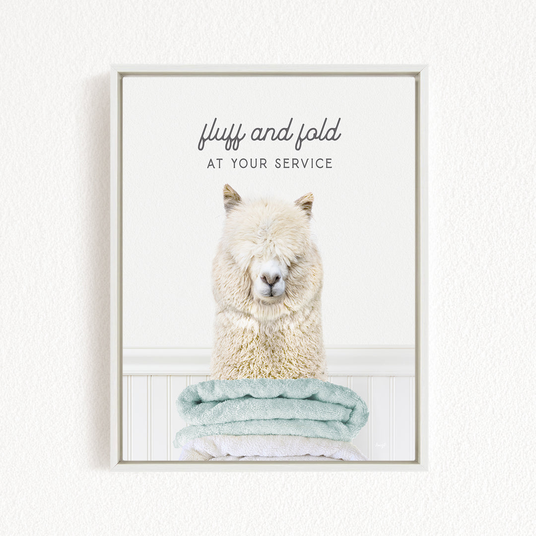 A fluffy alpaca sitting on a stack of light blue towels, with the text "fluff and fold at your service" above the image.