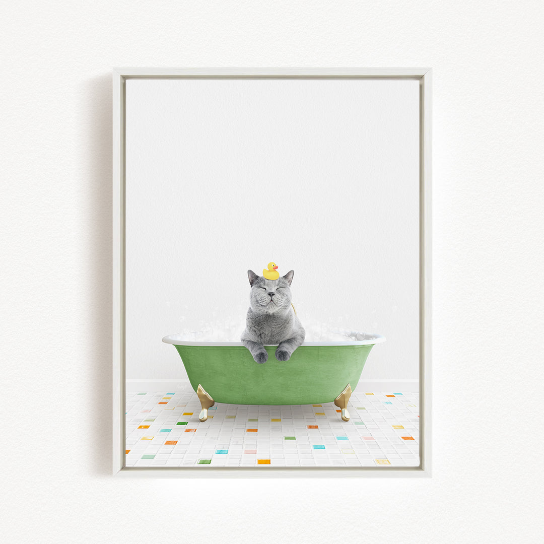 A gray cat sitting in a green bathtub filled with bubbles, with a yellow rubber duck on its head.
