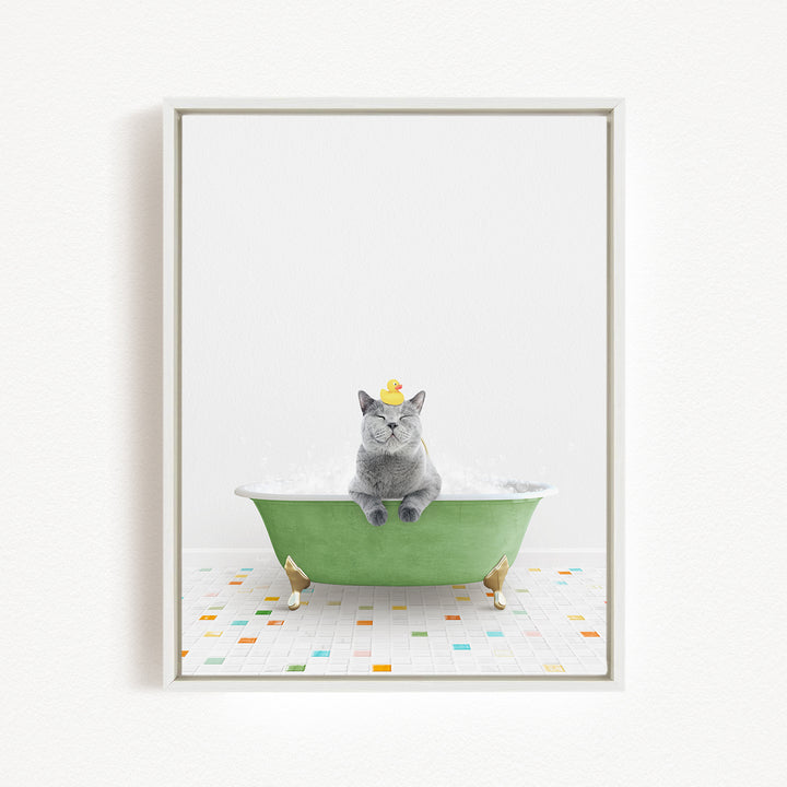 A gray cat sitting in a green bathtub filled with bubbles, with a yellow rubber duck on its head.