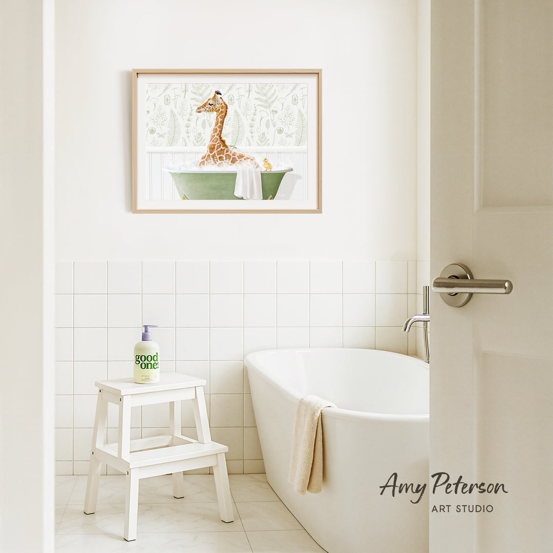 A framed painting of a giraffe sitting in a bathtub is hanging on a white tiled wall above a white bathtub in a bathroom.